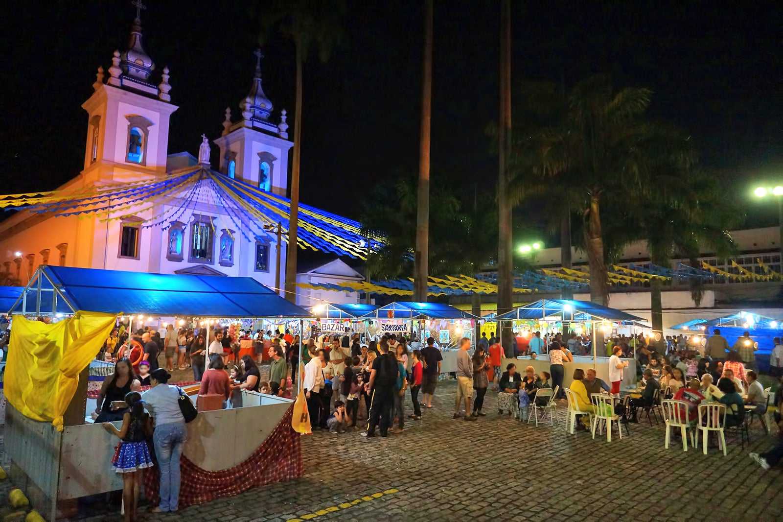 Festa junina noturna no Rio de Janeiro com barracas iluminadas, igreja ao fundo e bandeirinhas coloridas